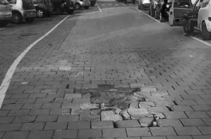 Strada in mattoni autobloccanti con buche e pavimentazione sollevata e dissestata, quartiere Muggiano